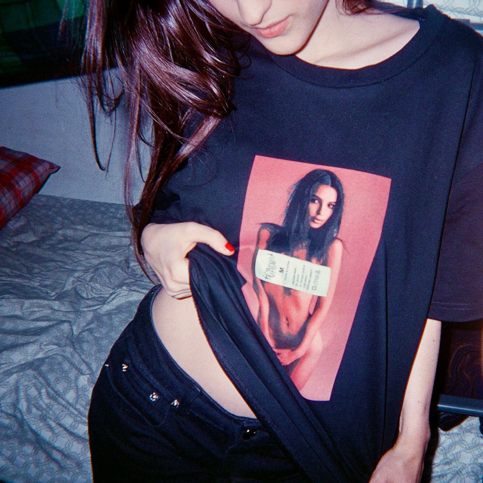 Person wearing a black t-shirt with a graphic design of a woman on it, sitting on a bed.