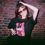Person wearing a black t-shirt with a graphic design in front of a brick wall