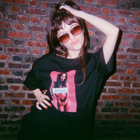 Person wearing a black t-shirt with a graphic design in front of a brick wall